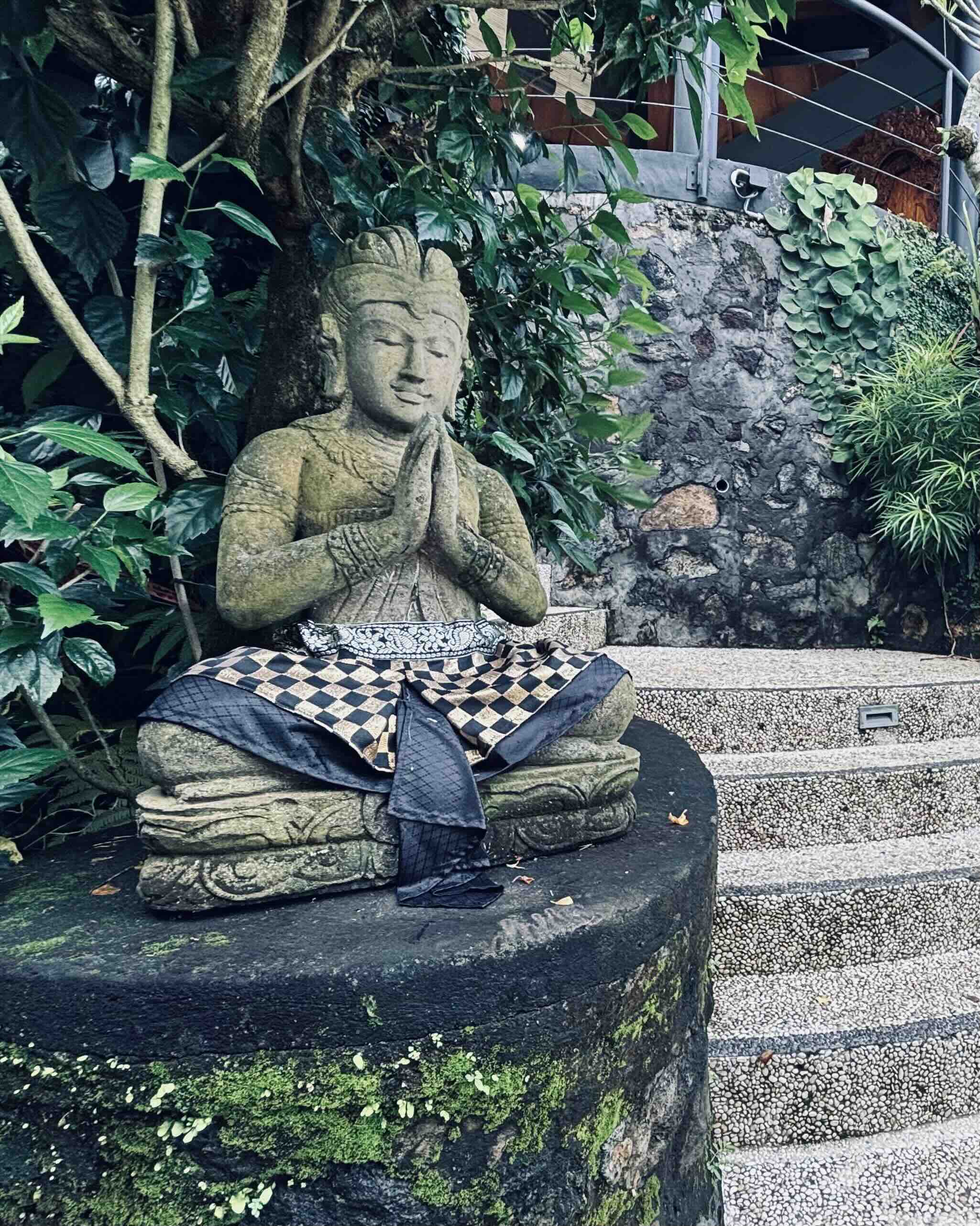 Balinese stone statue in prayer surrounded by tropical foliage